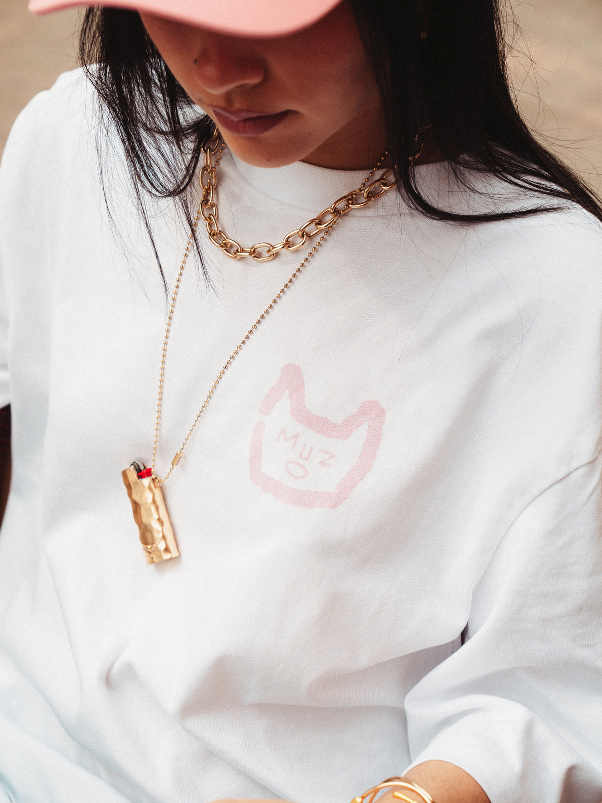 Zoom sur le coeur de Swan, logo muzo rose avec joli collier porte briquet doré.
T-shirt blanc dominant.